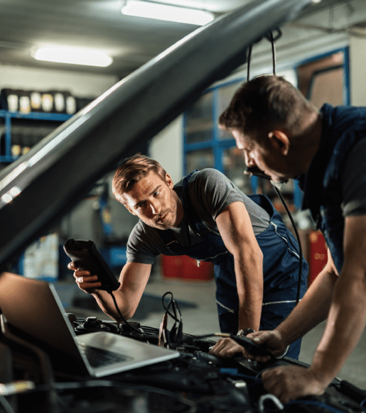 young car repairman talking with his coworker while checking engine performance with diagnostic tools auto repair shop